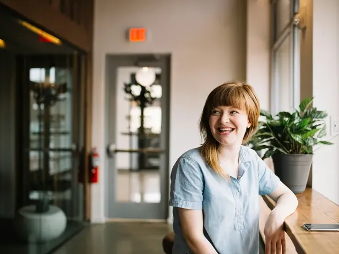 Smiling professional by a window in a workspace, showing friendly service and community links on CityNetworkHub